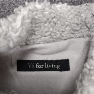 Op de afbeelding: Een close-up van een grijze fleecejas met een witte sherpa voering. Het label luidt "Y's for living".