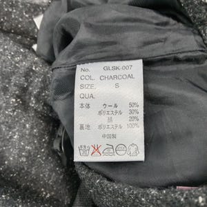 Pode incluir: Close-up de uma etiqueta de vestu&aacute;rio com o texto "GLSK-007 COL. CHARCOAL SIZE. S". A etiqueta lista a composi&ccedil;&atilde;o do tecido: l&atilde;, poli&eacute;ster e algod&atilde;o. As instru&ccedil;&otilde;es de lavagem tamb&eacute;m s&atilde;o vis&iacute;veis.