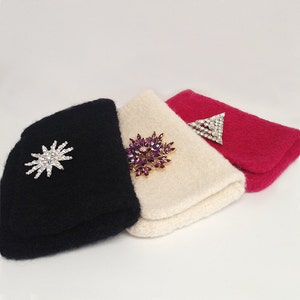 Peut inclure: Trois pochettes en tissu tricoté avec des embellissements différents. La première pochette est noire avec une broche en forme d'étoile argentée. La deuxième pochette est crème avec une broche violette et dorée. La troisième pochette est rouge avec une broche en forme de triangle argentée.