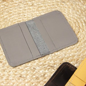 May include: A gray leather wallet with three card slots and a center pocket. The wallet is stitched with a light gray thread.