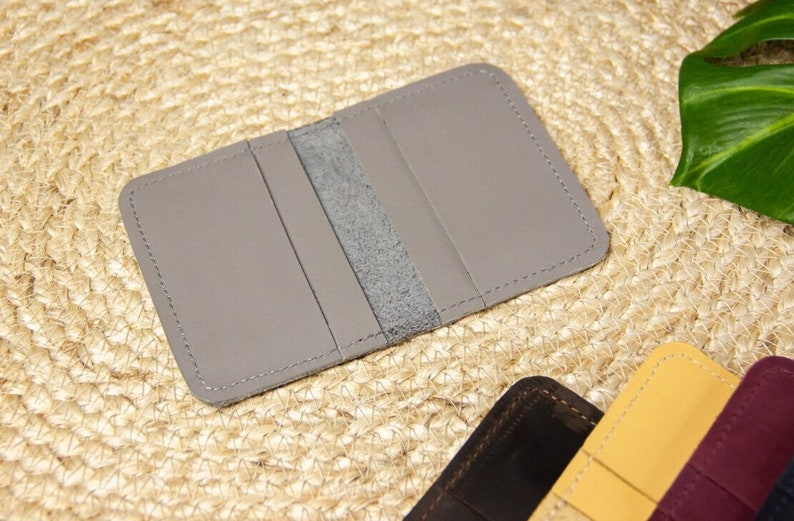 May include: A gray leather wallet with three card slots and a center pocket. The wallet is stitched with a light gray thread.