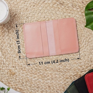 May include: A light pink leather card holder with three slots. The card holder measures 4.2 inches wide and 3 inches tall.