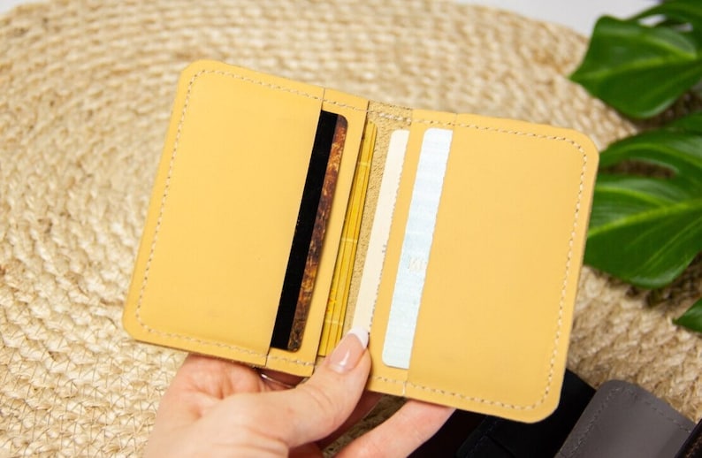 May include: A light yellow leather wallet with multiple card slots. The wallet is open and shows the interior card slots.