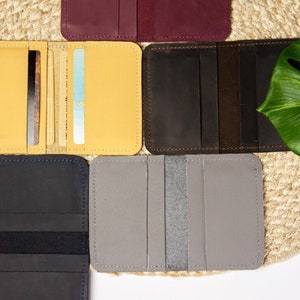 May include: Six different leather card holders in various colors, including yellow, brown, gray, black, and burgundy. The card holders are laid out on a woven straw surface.