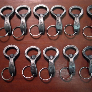 May include: Twelve silver bottle openers with keychains. Each opener has a different letter engraved on it.