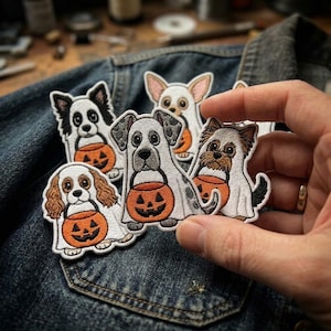 May include: A collection of five embroidered iron-on patches featuring various dog breeds dressed in white ghost costumes, each holding an orange jack-o'-lantern candy bucket. The patches display detailed stitching of different canine faces.