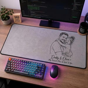 May include: A gray rectangular desk mat with a black border, featuring a sketch of a father and child with the text "Daddy & Olivia My Favorite Place Is Next To You". A keyboard and mouse are in the foreground.