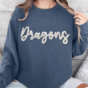 May include: A blue sweatshirt with a white fluffy embroidered word "Dragons" on the front.