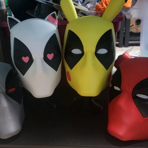 May include: Four Deadpool masks, one white with pink hearts, one yellow, one gray, and one red.
