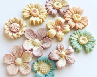 May include: A collection of colorful, flower-shaped cookies. The cookies are in various pastel colors, including yellow, pink, and blue, with detailed petal and center designs. The cookies are arranged on a white surface.