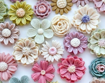 May include: A collection of colorful, decorative flower embellishments in various shapes and sizes. The flowers are in shades of pink, purple, yellow, green, and white. Some have textured centers, and others have smooth petals. These are likely for crafts.