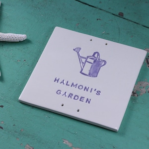 May include: White ceramic garden sign with purple lettering that reads "Halmoni's Garden". A purple watering can with a flower is above the text.