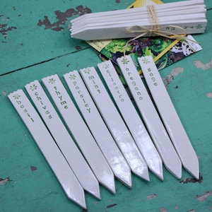 May include: White plant markers with green lettering, including the words "basil", "chives", "thyme", "parsley", "mint", "cilantro", "oregano", and "sage".