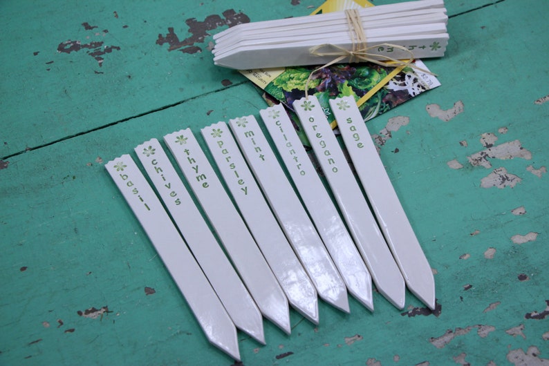 May include: White plant markers with green lettering, including the words "basil", "chives", "thyme", "parsley", "mint", "cilantro", "oregano", and "sage".