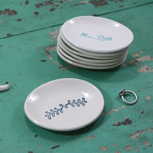 May include: A set of five white ceramic ring dishes with a blue floral design. The dishes are stacked on top of each other. A single ring dish is on the table next to the stack.