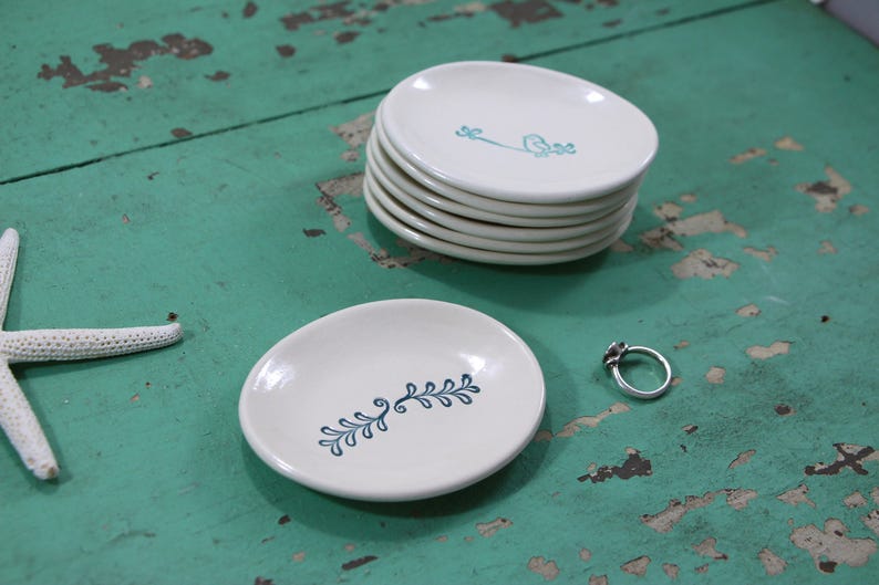 May include: A set of five white ceramic ring dishes with a blue floral design. The dishes are stacked on top of each other. A single ring dish is on the table next to the stack.