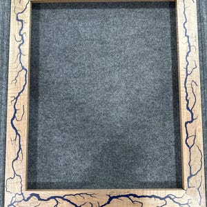 Pode incluir: Uma moldura de madeira com uma incrustação de resina azul que se assemelha a um padrão de raio.
