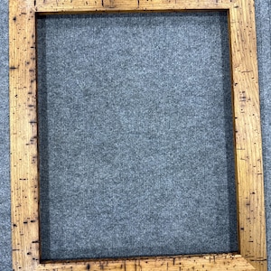 Può includere: Una cornice rettangolare con finitura in legno marrone chiaro caratterizzata da un evidente motivo a macchie marrone scuro su tutta la superficie. La cornice presenta quattro angoli a 45 gradi e un bordo piatto e largo con un'apertura.