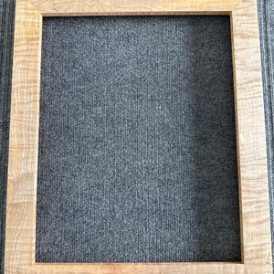 Pode incluir: Uma moldura retangular de madeira com acabamento natural de grão. A moldura é feita de madeira clara e tem um design simples e clássico. A moldura está vazia, pronta para conter uma fotografia ou uma obra de arte.