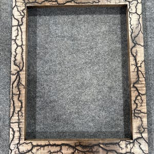 Könnte beinhalten: Ein Holzbildrahmen mit einer dunkelbraunen Oberfläche und einem einzigartigen schwarzen Blitzdesign.