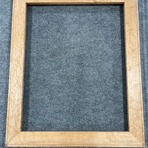 Pode incluir: Uma moldura de imagem de madeira natural com acabamento marrom claro. A moldura tem um design simples e retangular e é feita de madeira maciça.