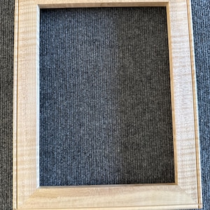 May include: A rectangular, unfinished wooden picture frame. The frame is made of light-colored wood with a natural grain pattern. The frame has a simple, classic design, with a flat surface and a recessed inner edge.