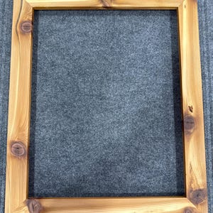 Könnte beinhalten: Ein quadratischer Holzbilderrahmen mit natürlicher Oberfläche. Der Rahmen besteht aus hellfarbenem Holz mit sichtbaren Knoten und Maserungsmustern. Der Rahmen ist leer, ohne Bild oder Kunstwerk darin.