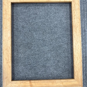 May include: A rectangular picture frame constructed from light-colored wood with a visible natural grain pattern. The frame features mitered corners and a flat, wide border profile, showcasing a smooth finish and consistent light brown tones.