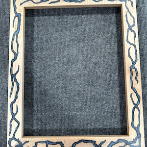 May include: A wooden picture frame with a black resin inlay that resembles a lightning bolt pattern.