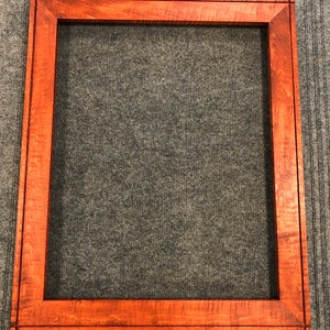 Pode incluir: Uma moldura de imagem retangular de madeira com um rico tom marrom avermelhado. A moldura tem um design simples e clássico com um acabamento liso.