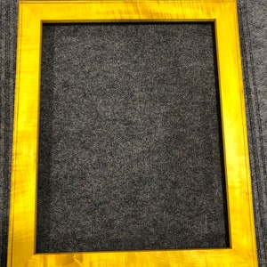 Puede incluir: Un marco de imagen de madera amarilla con un acabado liso y pulido. El marco tiene un diseño simple y rectangular.