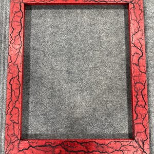 May include: A red picture frame with a black crackle finish. The frame is made of wood and has a rectangular shape.