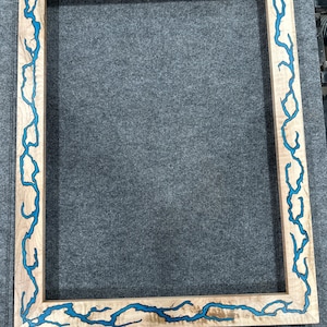 以下が含まれることがあります： 渦巻き模様の青い樹脂製のインレイが施された木製の写真フレーム。フレームは自然な木でできており、明るい茶色の仕上げになっています。