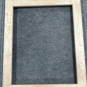 Puede incluir: Un marco de imagen de madera natural con un acabado marrón claro. El marco tiene un diseño simple y rectangular y está hecho de madera maciza.