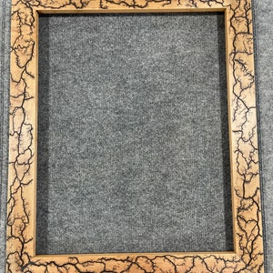 Pode incluir: Uma moldura de madeira para fotos com um design único de madeira queimada. A moldura é de cor marrom escura com uma veia de madeira marrom clara. A moldura é retangular e tem um design simples.