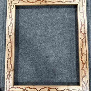 Pode incluir: Uma moldura de madeira com acabamento em madeira natural e uma borda decorativa laranja e marrom. A borda apresenta um design único de linhas ramificadas.