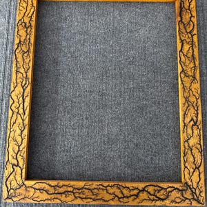 Pode incluir: Uma moldura quadrada de madeira com acabamento natural. A moldura é decorada com um padrão preto, semelhante a um fractal, que se assemelha a galhos de árvores ou raios. A moldura está vazia, pronta para uma foto ou obra de arte.