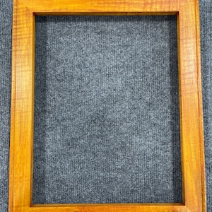 May include: A wooden picture frame with a natural wood finish. The frame is rectangular and has a simple design.