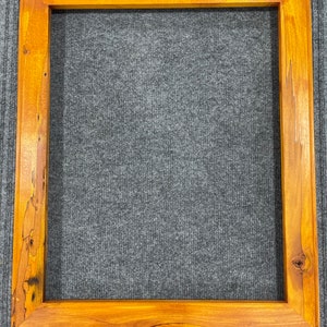 Pode incluir: Uma moldura quadrada de madeira com um acabamento castanho-dourado quente. A moldura tem um design simples e clássico com grão de madeira e nós visíveis, adicionando um toque natural e rústico. A moldura está vazia, pronta para uma foto ou obra de arte.