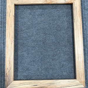 Puede incluir: Un marco de imagen de madera natural con un acabado marrón claro y veta de madera marrón oscuro. El marco tiene un diseño simple y rectangular.