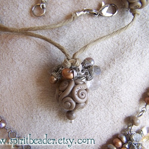 May include: A brown and beige necklace with a large, swirl-shaped pendant. The pendant is made of clay and has a textured surface. The necklace is made of twine and has a silver clasp.