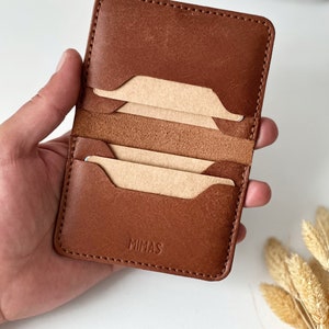 May include: A brown leather card holder with three card slots and the word "MIMAS" embossed on the front.