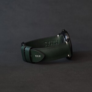 May include: A dark green leather watch strap with white stitching and the word "Miras" embossed on the strap.