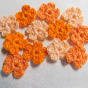 May include: A collection of crocheted flowers in shades of orange and peach. The flowers are arranged in a cluster on a white background.