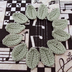 May include: A set of twelve crocheted green leaf shapes arranged in a circle. The leaves are made with a textured stitch and have a slightly rounded shape.