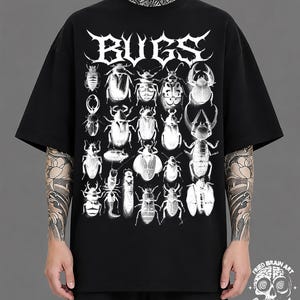 Può includere: Una t-shirt nera a maniche corte con una grande stampa grafica bianca di varie illustrazioni di insetti disposte a griglia. La parola BUGS è stampata in un carattere bianco stilizzato e frastagliato nella parte superiore.