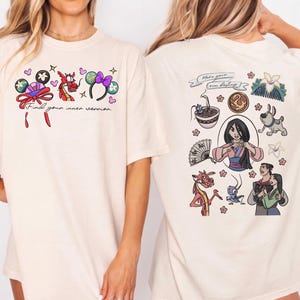 Puede incluir: Camiseta color crema con gráficos de dibujos animados coloridos y texto. La parte delantera muestra la frase "Find your inner warrior" con varias ilustraciones. La parte trasera muestra arte de personajes adicionales y el texto "Make your own destiny."
