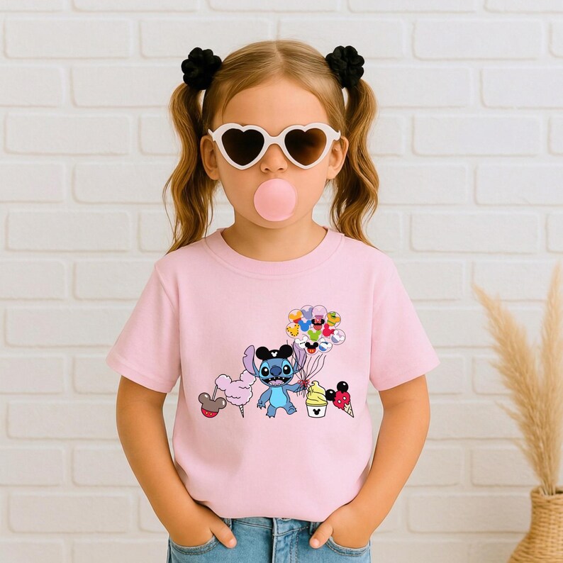 Puede incluir: Camiseta rosa claro con un personaje de dibujos animados Stitch sosteniendo globos, algod&oacute;n de az&uacute;car y conos de helado. El gr&aacute;fico es de colores brillantes. La camiseta la lleva una persona joven con gafas de sol en forma de coraz&oacute;n y lazos negros para el pelo.