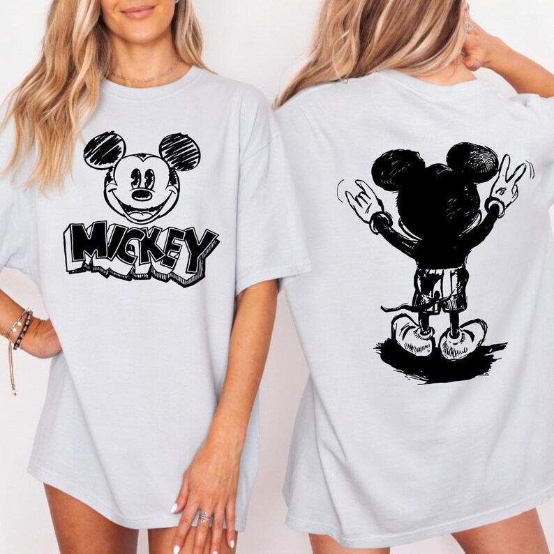 May include: Light blue t-shirt featuring a black and white Mickey Mouse graphic on the front and back. The front design includes Mickey's face and the word "Mickey". The back design shows Mickey with his arms raised in a rock and roll gesture.