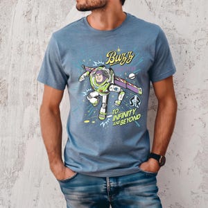 May include: Blue t-shirt featuring a graphic of Buzz Lightyear from Toy Story. The design includes the text "Buzz" and "To Infinity and Beyond" with a space-themed background. The shirt is made of a soft material.